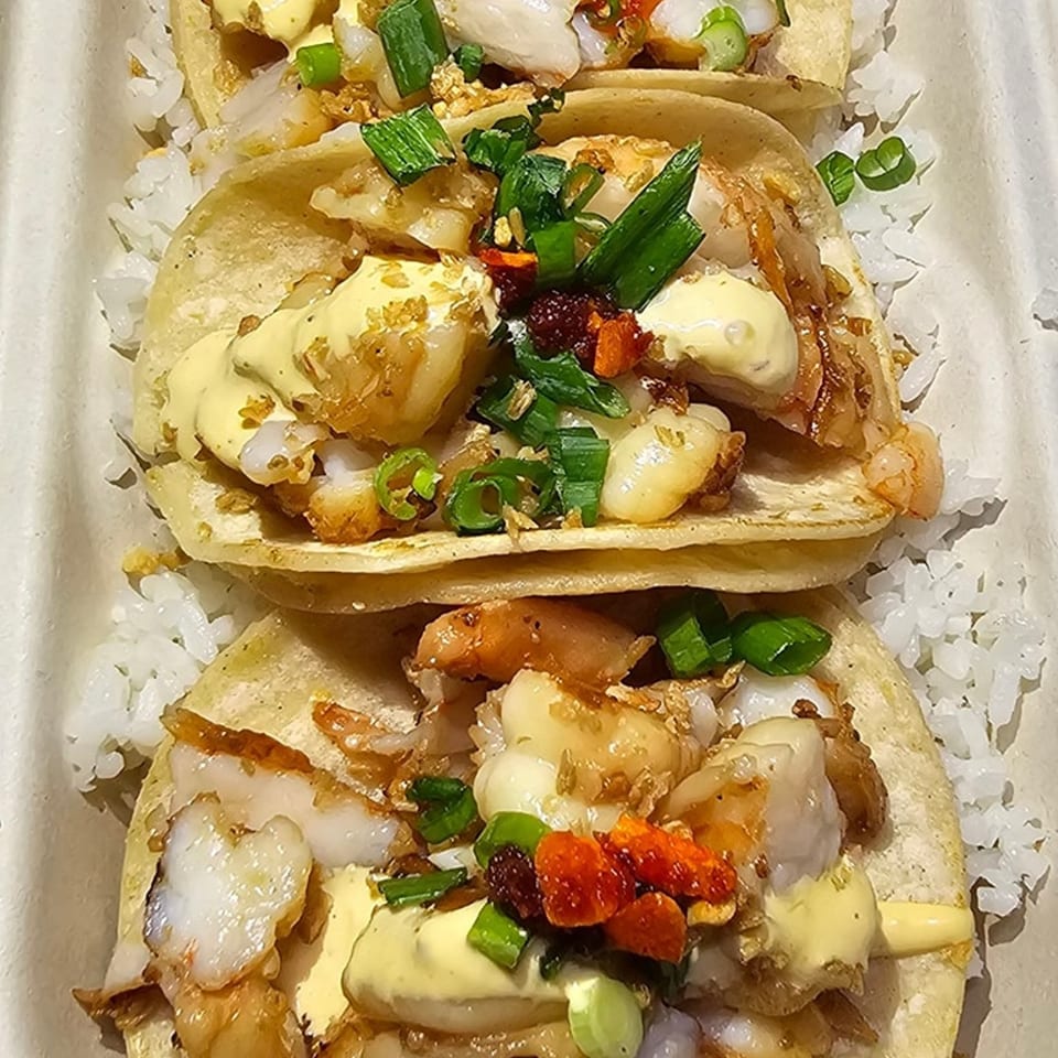 Three Truk N Yaki shrimp tacos with sauce, green onions, and rice in a container.