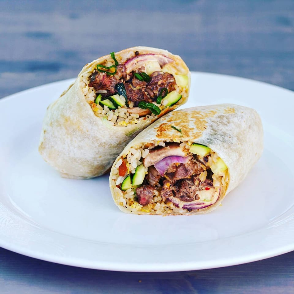 Two halves of a Truk N Yaki Japanese burrito filled with meat, rice, zucchini, and red onion.
